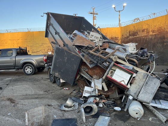 Our dump trailer tipping a load of scrap appliances at a Los Angeles County metal yard: stoves, air-conditioning units, a water heater and mixed steel sliding out onto the floor