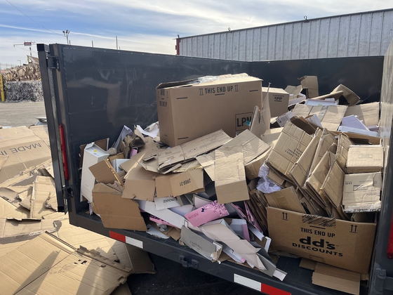 The bed of our dump trailer filled to the rail with flattened cardboard cartons and packing waste from a retail clear-out, parked at a Los Angeles County recycling facility