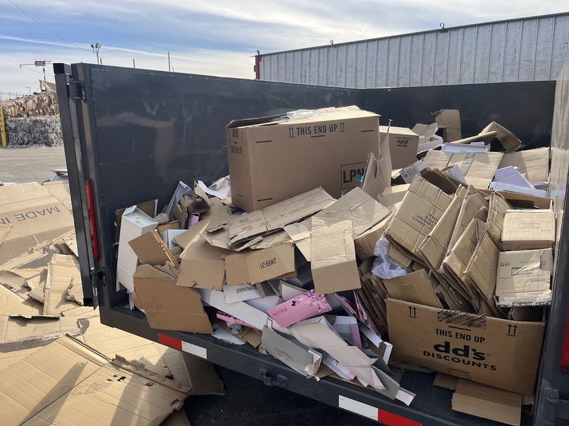 The bed of our dump trailer filled to the rail with flattened cardboard cartons and packing waste from a retail clear-out, parked at a Los Angeles County recycling facility