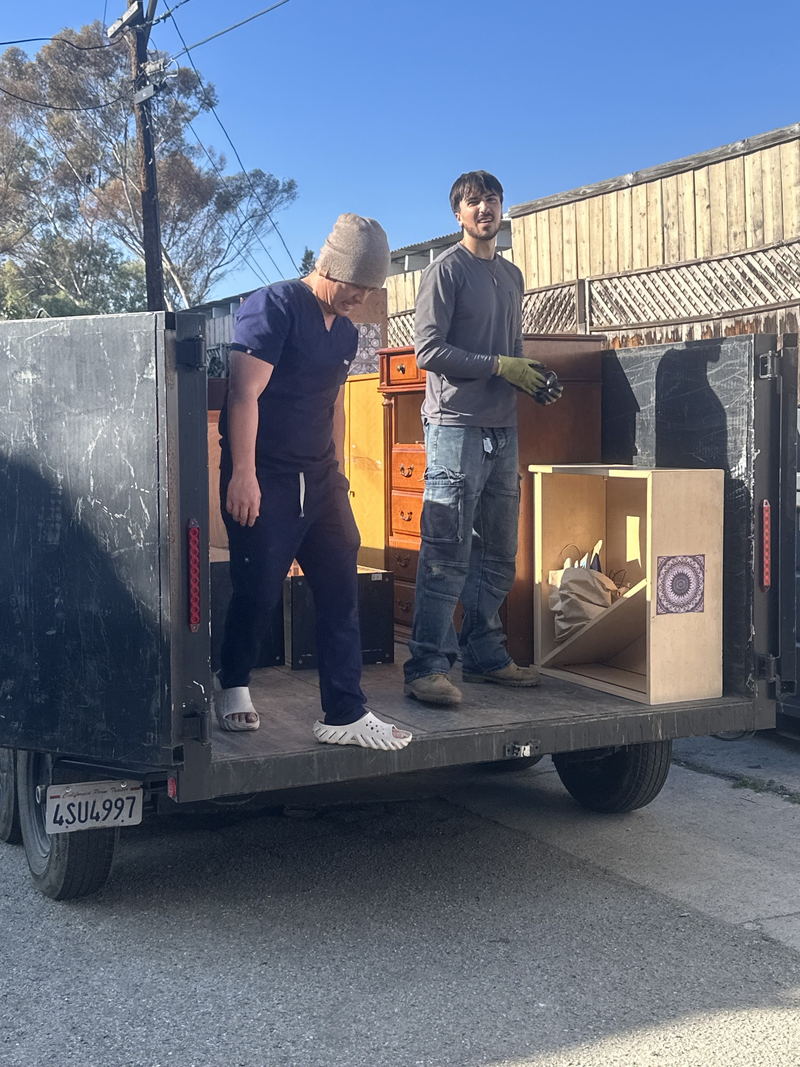 Two of our crew standing on the deck of the dump trailer on a Los Angeles County job, working a timber chest of drawers and a cabinet into place by hand