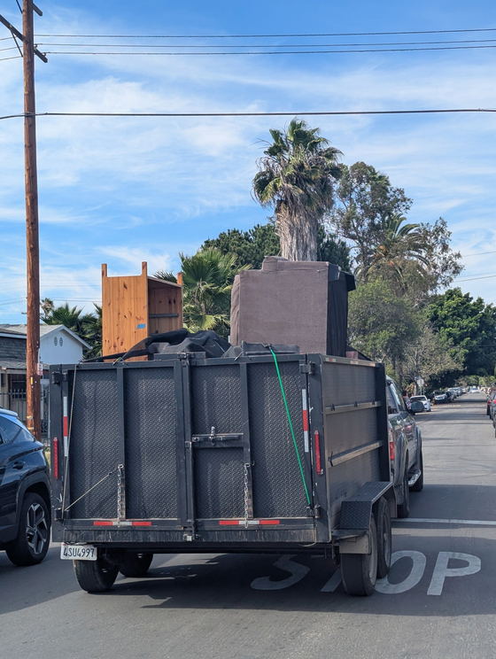 Our dump trailer pulling away down a palm-lined Los Angeles County street with a timber chest of drawers and a gray upholstered armchair strapped upright in the bed