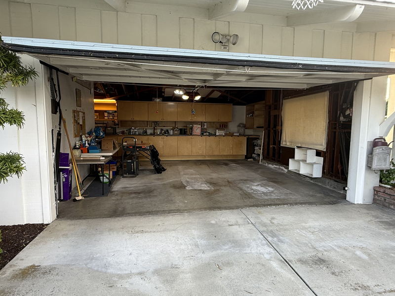 A two-car Los Angeles County garage after a full clear-out, the slab swept empty with only the workbench and wall cabinets left in place and the door open to the driveway