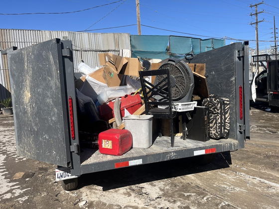 Our dump trailer loaded with a mixed household clear-out on a Los Angeles County job: an office chair, a pedestal fan, a cooler, suitcases, a fuel can and cartons stacked against the headboard