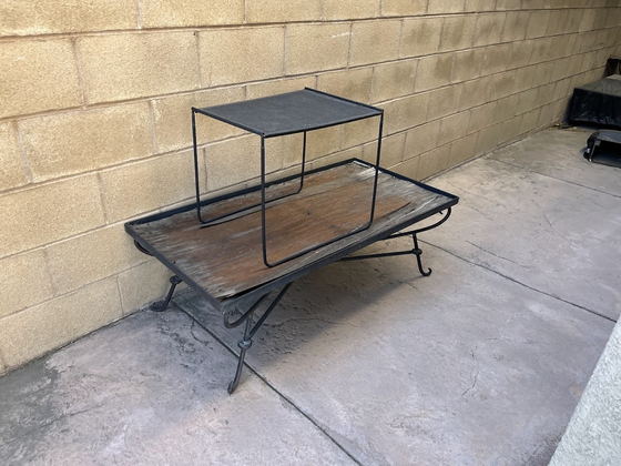 A weathered wrought-iron and timber coffee table and matching side table set out against a block wall on a Los Angeles County patio, waiting to be lifted away