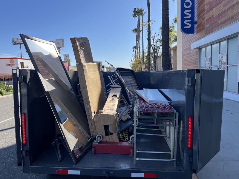 Our dump trailer loaded outside a Los Angeles County retail unit with flat-pack furniture cartons, steel gondola shelving, a stock trolley and display racking