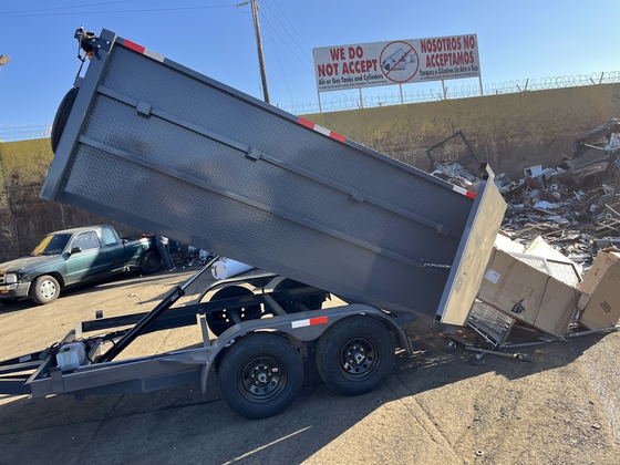 Our empty dump trailer tipped up beside a scrap pile at a Los Angeles County transfer station, under the yard sign refusing air and gas cylinders