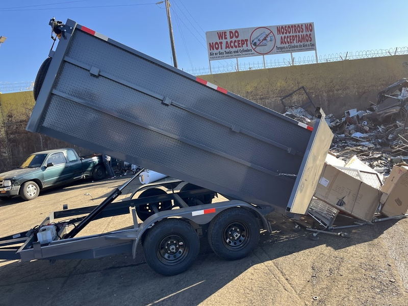 Our empty dump trailer tipped up beside a scrap pile at a Los Angeles County transfer station, under the yard sign refusing air and gas cylinders